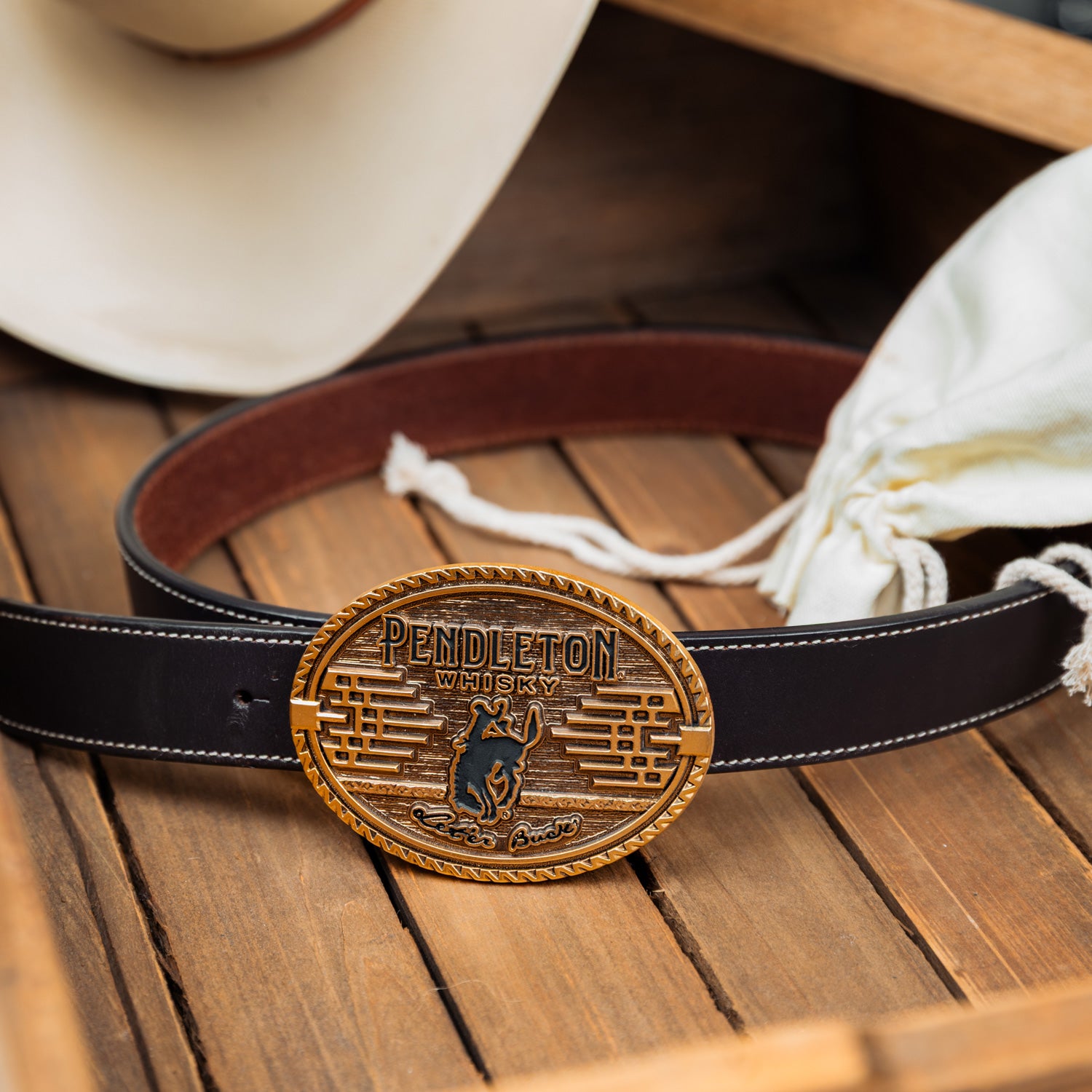 Image of the 2026 Pendleton Whisky Belt Buckle on a belt on top of a wooden box