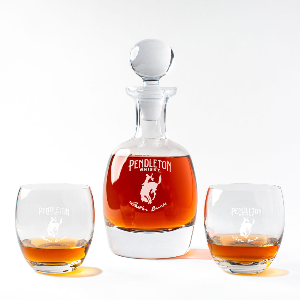 A crystal decanter with a Pendleton Whiskey logo and two rocks glasses, also with the Pendleton logo, on a white background.