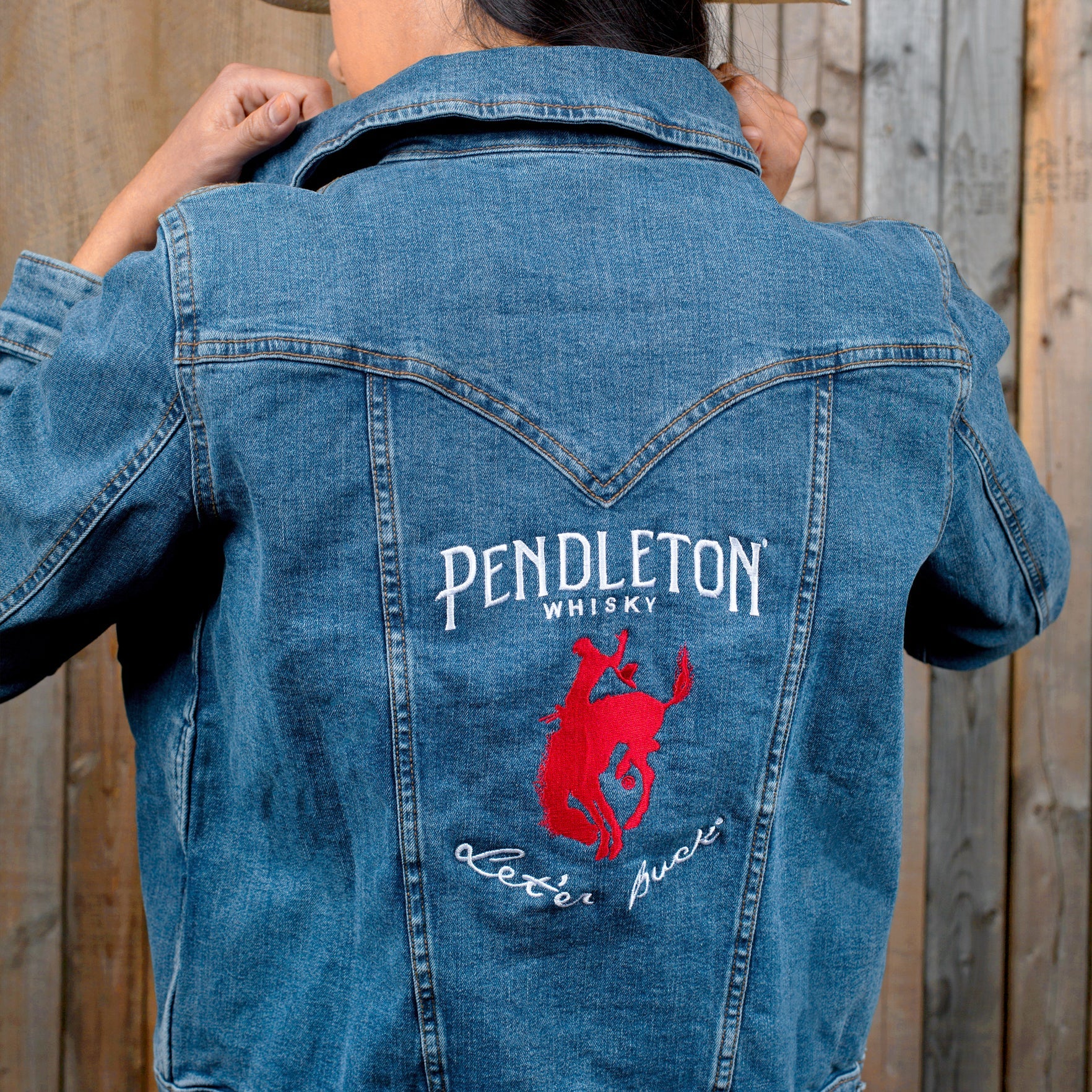 Back view of a woman wearing a Wrangler Denim Jacket with the Pendleton®️ Whisky logo embroidered on the pack panel 