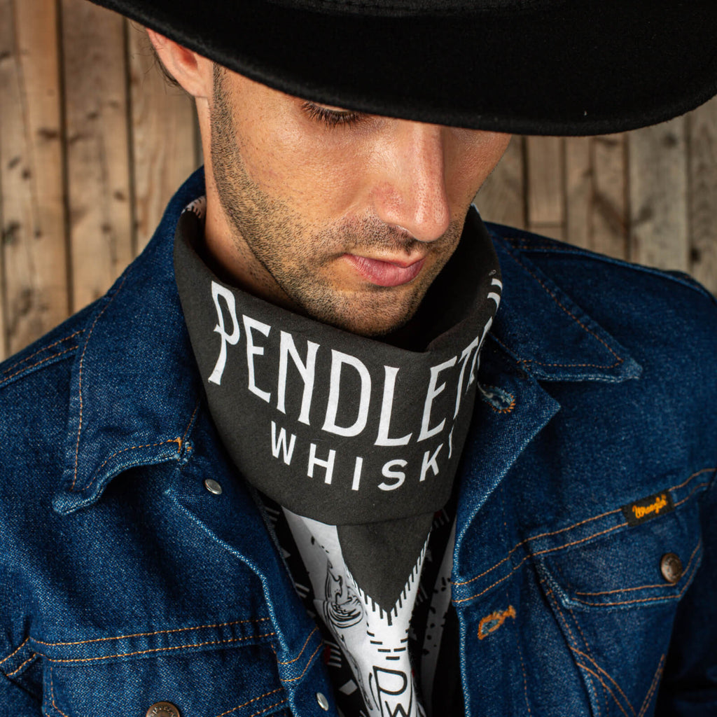 Man wearing black cowboy hat, jean jacket, and black, red, and white patterned Pendleton® Whisky Bandana around his neck