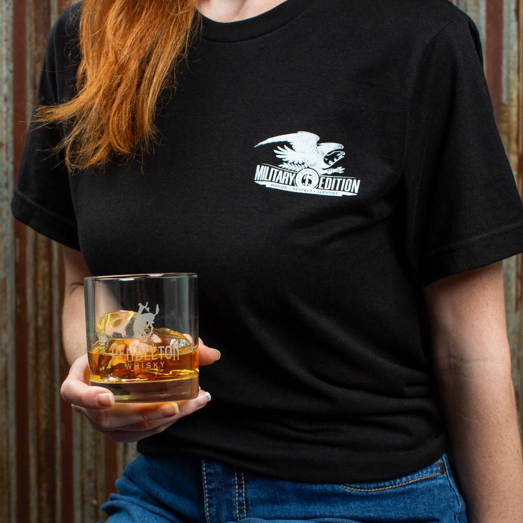 Woman wearing Military Edition T-shirt holding a rocks glass.
